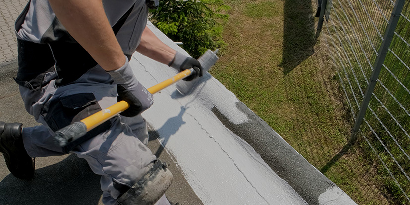 Ein fleißiger Handwerker trägt eine Schicht Flachdachabdichtung auf ein Garagendach au